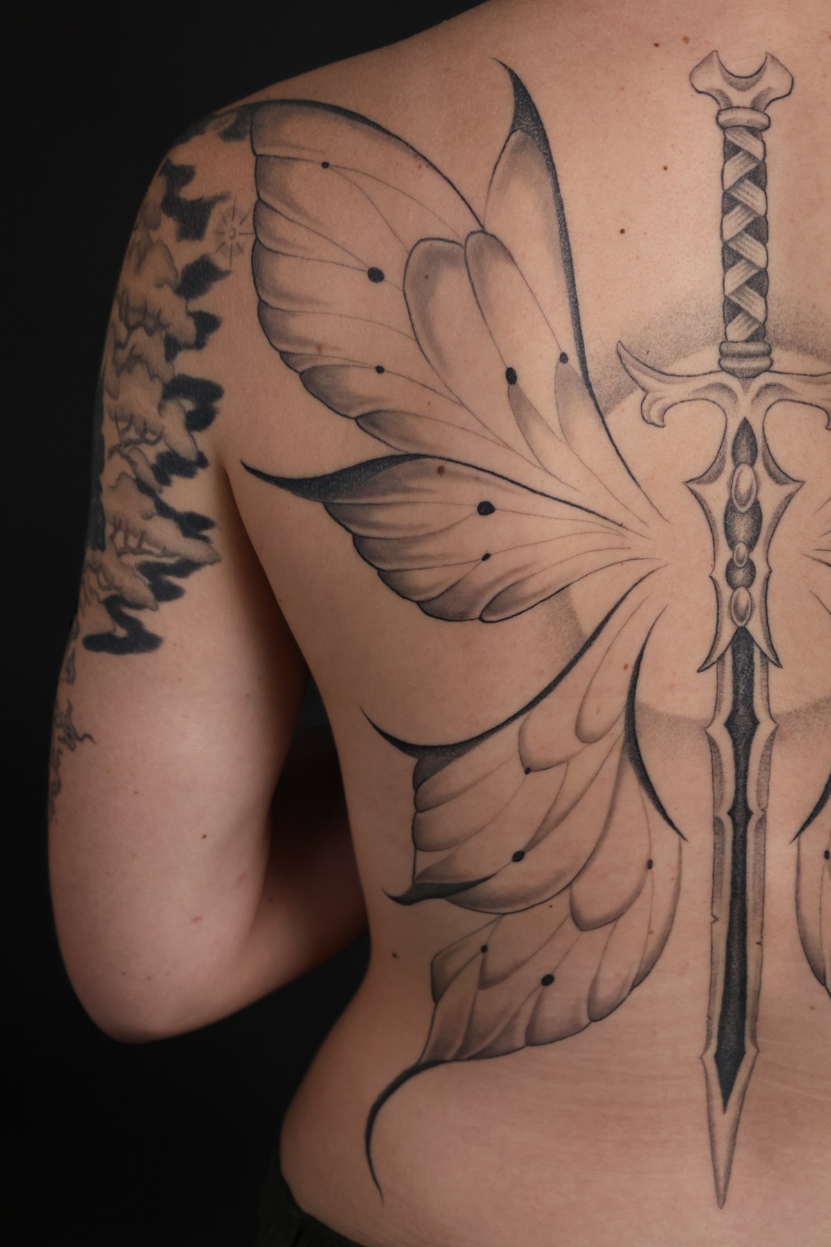 Fine line back tattoo with butterfly wings and a sword