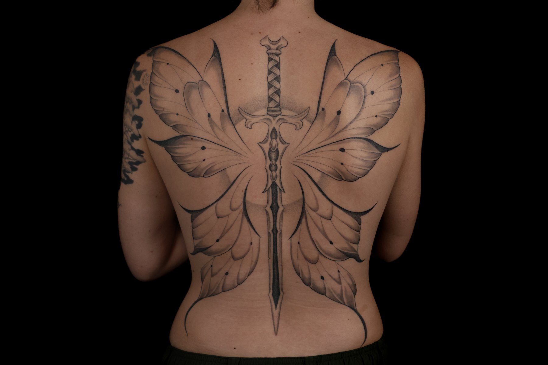 Fine line sword and butterfly wings tattoo across the back