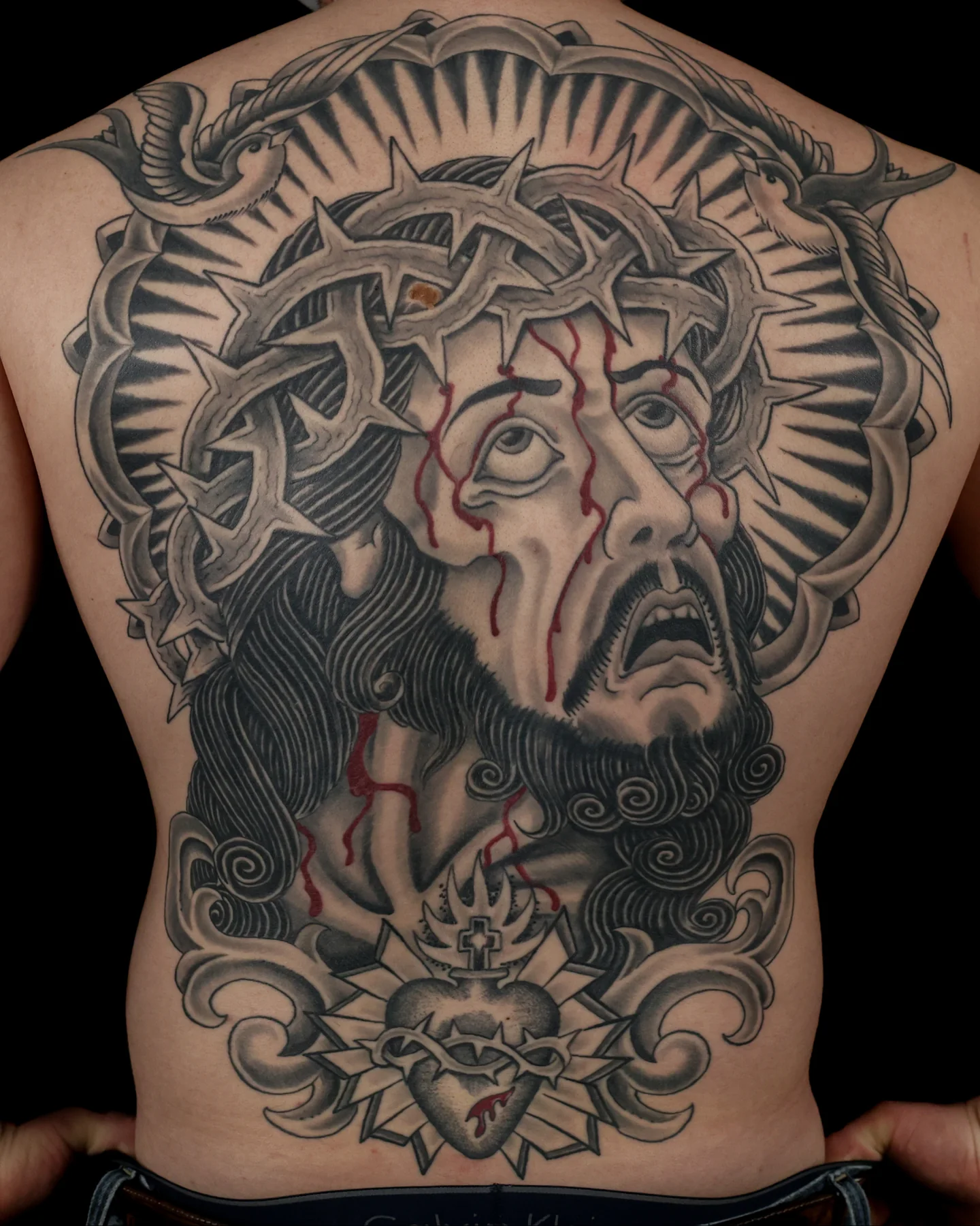 Black and grey back tattoo with a bearded face by Angel Serda